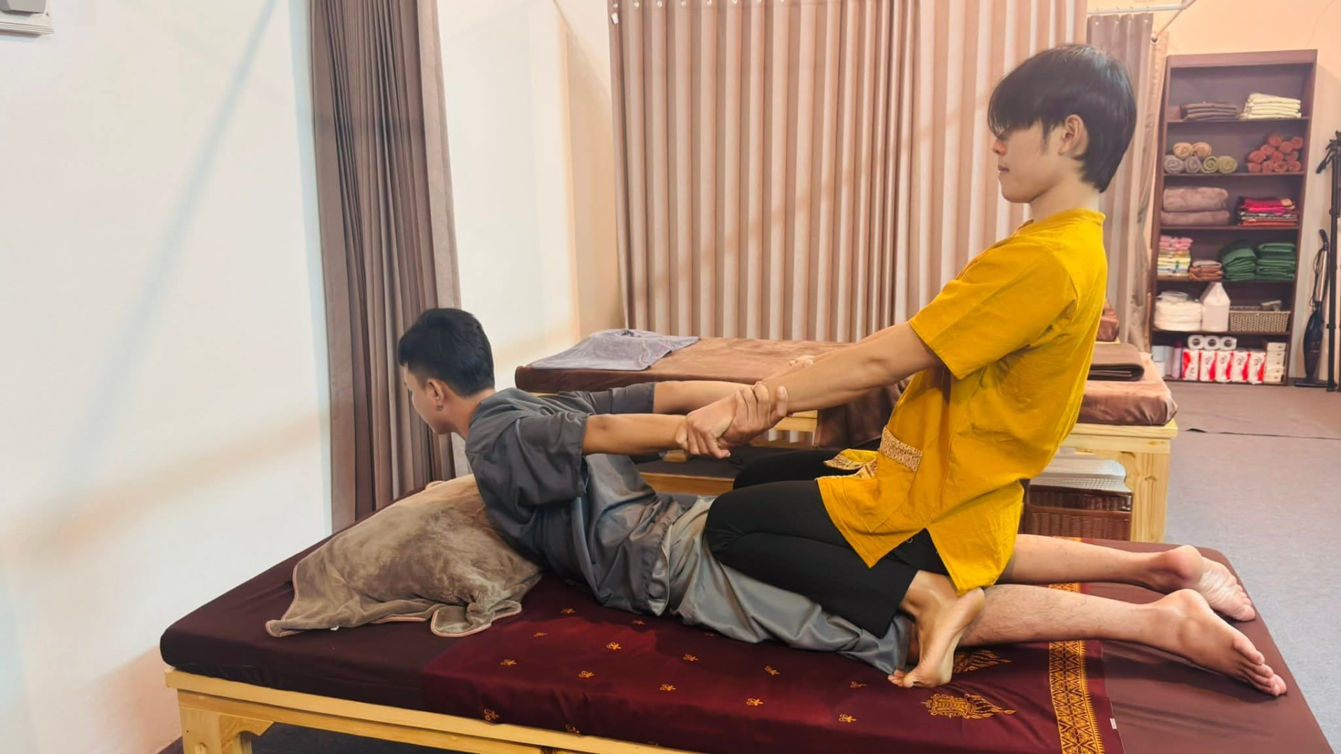 หมอนวดน้ำทิพย์สาธิตท่านวดไทยยืดเส้นให้ลูกค้าบนเตียงนวด